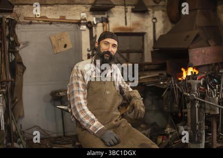 Bearded blacksmith after working in his workshop. Blacksmith's workshop. Professional blacksmith man portrait Stock Photo