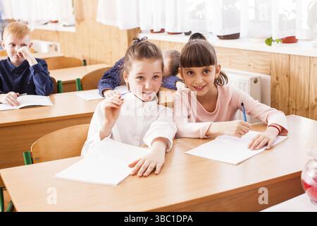 Portrait of two girlfriends who sitting at the same desk in the classroom Stock Photo