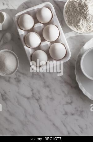 Top view ceramic tray with eggs placed near bowl of flour and sugar. White utensils with white ingredients on white surface. Copy space Stock Photo