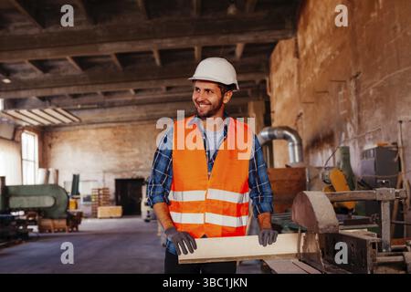 Portrait of happy young foreman with hard hat and protective gloves work with wooden boards Stock Photo