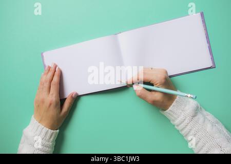 Overhead open sketchbook with blank pages. Woman in white, holding pencil preparing to draw. Light turquoise background, copy space Stock Photo