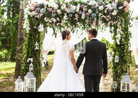Beauty wedding couple under flower arch. Look from the back Stock Photo