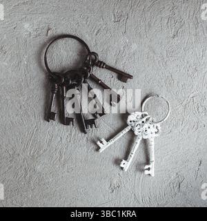 A bunch of vintage metal keys on ring hanging on the screw on the grey concrete background Stock Photo