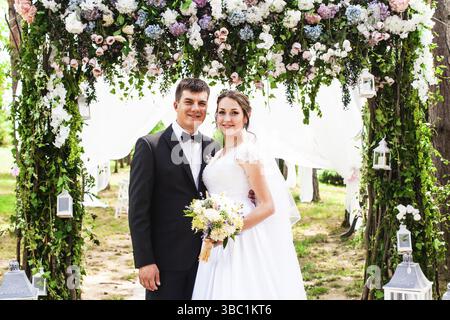 Adorable beauty wedding couple under flower arch. Wedding holiday decorations outdoor Stock Photo