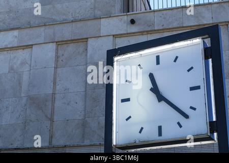 Close-up of a large white clock with blue hands indicating the time against a marble building wall Stock Photo