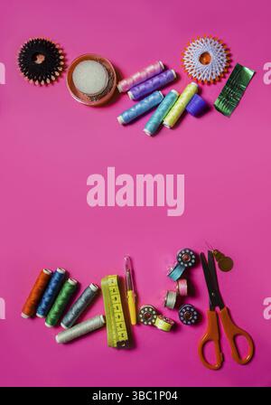 Several spools with cotton threads placed with scissors and set of needles on pink surface. Set of non-professional sewing instruments. Copy space Stock Photo