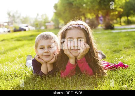 Picture of brother and sister having fun in the park, two cheerful children laying down on green grass Stock Photo