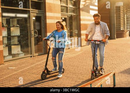 The young couple of diverse people are riding on electric scooters around the city in summertime Stock Photo