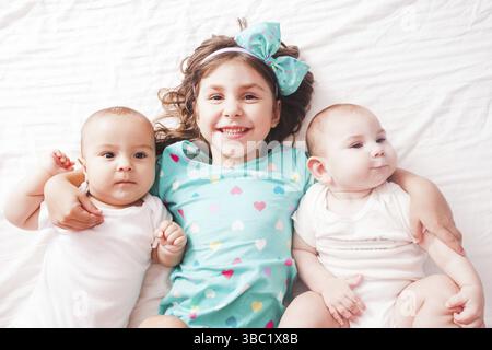 Five years old girl with her brothers - twins lying on the bed Stock Photo