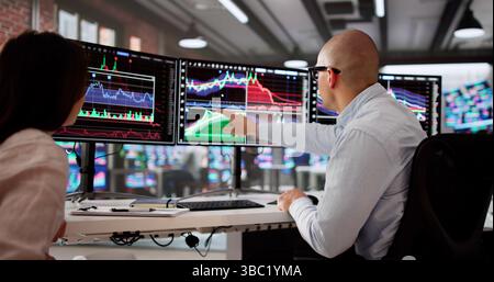 Team Of Young Stock Brokers Analyze Graphs On Computer Screens. Stock Photo