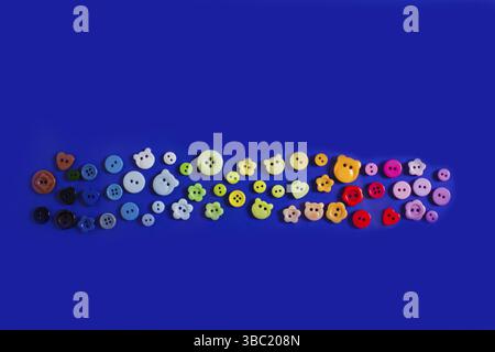 Top view flat-lay variety of buttons in different shapes, sizes and colors. Rainbow colors buttons on trendy blue background Stock Photo