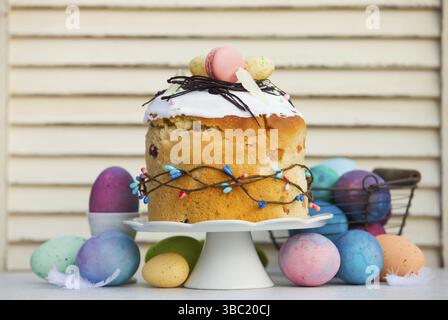 Professionaly baked traditional Easter bread - paska with stylish decoration on top. Multicilor eggs around cake stand with Easter bread on it. Spring Stock Photo
