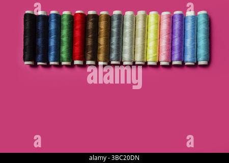 Straight row of spools with different colours threads, flat lay on pink background. Assortment of colors for best choice. Top view, copy space Stock Photo