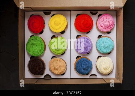 Colourfull rainbow cupcakes in the box, top view on the black slate background Stock Photo