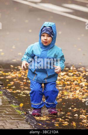 .Child in rubber boots and raincoat playing in a puddle Stock Photo - Alamy