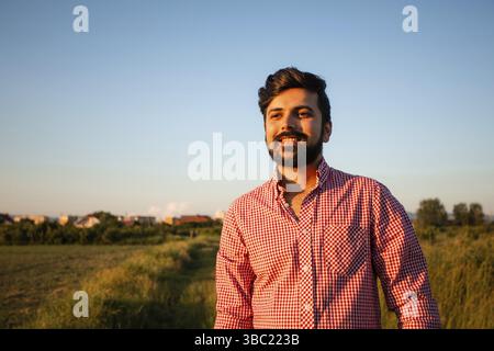 Happy young man posing outdoor on summer field background. Handsome bearded man in pink sunglasses enjoying summer sun outdoors in countryside Stock Photo