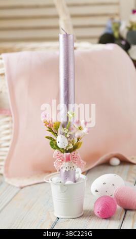One purple candle in small white can, used as candlestick, decorated with little artificial flowers. Few easter eggs placed near. Pink festive napkin Stock Photo