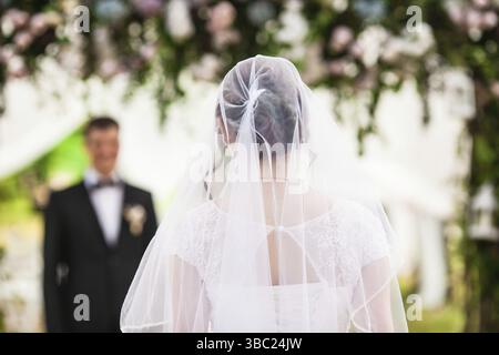Look from behind at groom that admires and waits for a charming bride. She is walking down the aisle Stock Photo