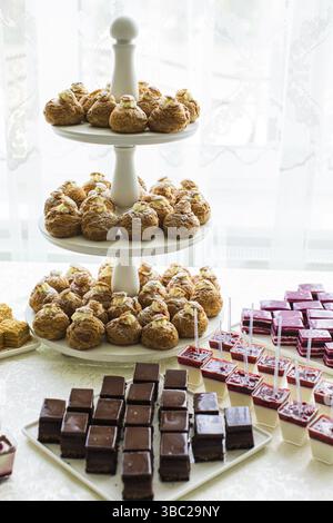 The wonderful cupcakes are laid out on a three-story white stand and many other desserts are located on a white table Stock Photo