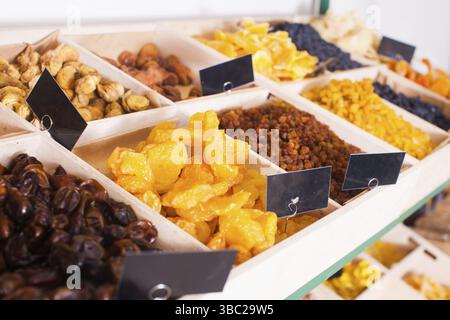 Close view of assortment of dry apricots, raisins, pears, dates, figs laying out on the rack with wooden boxes and black price tags. Self-service shop Stock Photo