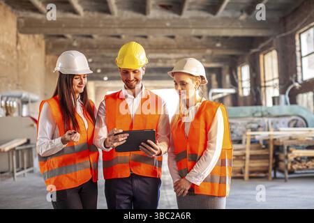 Team of young construction workers discussing project details with executive supervisor. Professional people with helmets Stock Photo