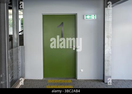 Green fire exit door number one with illuminated sign showing escape route and tactile paving, in modern building Stock Photo