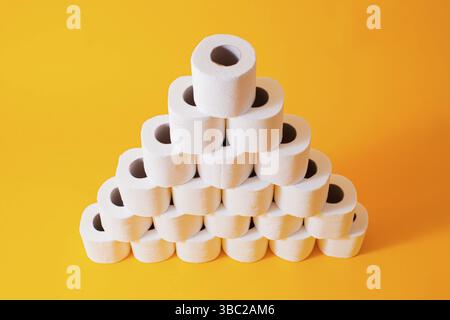 Pyramid created from white toilet paper rolls isolated on yellow. Symbol of quarantine Stock Photo
