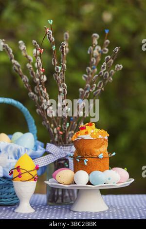 Close up picture of table with Easter decoration. Homemade Easter bread with icing and colored eggs on a white plate, yellow candle, decorated blue ba Stock Photo