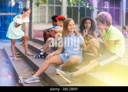 Positive tweenagers friendly blabbing while sitting on steps outdoors Stock Photo