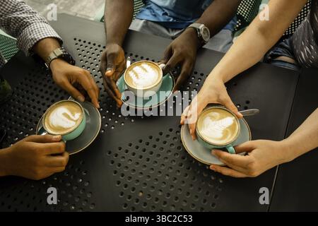 Top view unrecognised people's hands, holding cups of coffee on black background. People sitting around table drinking coffee showing idea of unity. D Stock Photo