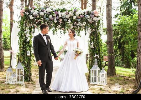 Adorable beauty wedding couple under flower arch. Wedding holiday decorations outdoor Stock Photo