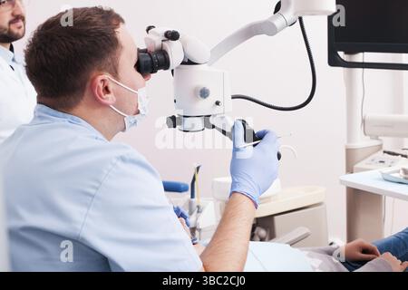 Dentist looking through magnifying glass. He's using microscope for operation at dentist office Stock Photo