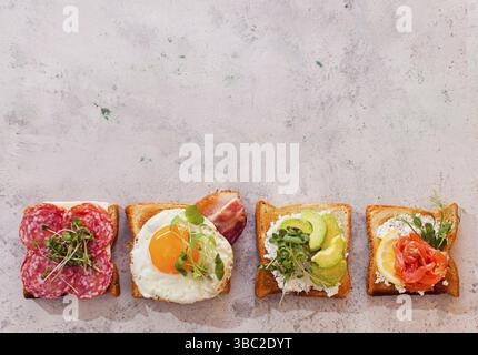 Set of delicious sandviches placed at the bottom part of photo. Fried toast bread, spreaded with cream spread and different ingredients on top. Variou Stock Photo