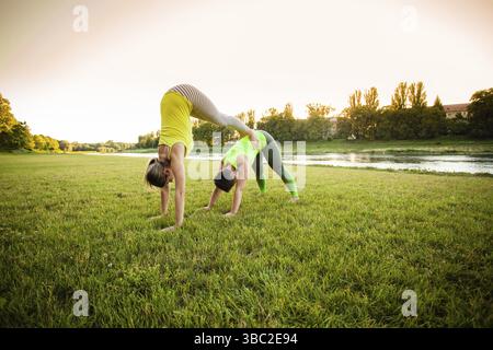 Two young beautiful women doing yoga standing in acro yoga pose. Healthy lifestyle modern activity Stock Photo