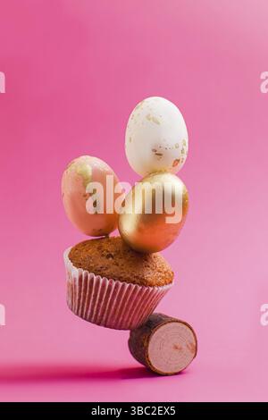 One small cupcake decorated with golden egg balancing on wooden roll. Sweet Easter composition, isolated on pink background Stock Photo