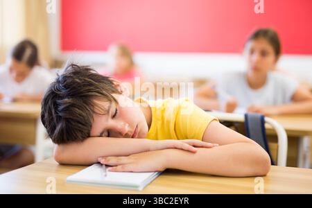 Tired preteen schoolboy sleeping at desk in classroom Stock Photo