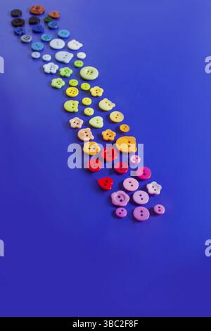 Top view path like set of multicolor buttons of different shapes and sizes on trendy blue surface. Tailors collection of buttons Stock Photo