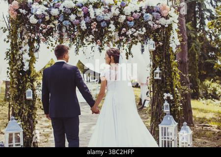 Beauty wedding couple under flower arch. Look from the back Stock Photo