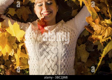 Woman laying in maple leaves in the park. Sunny warm day and fall foliage Stock Photo