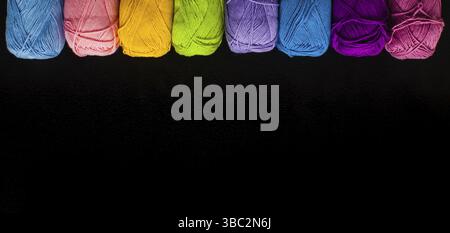 Top view row of rainbow yarn balls on the black background. Copy space for border design with threads in a row Stock Photo
