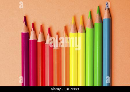 The wooden colored pencils in neon colors are arranged in a wave on an orange background Stock Photo