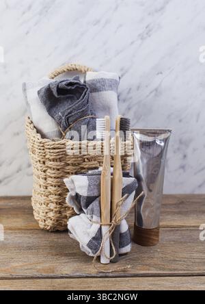 Smal straw basket filled with black and white towels. Two bamboo toothbrushes tied up in front of basket, with toothpaste in metal grey tube placed ne Stock Photo