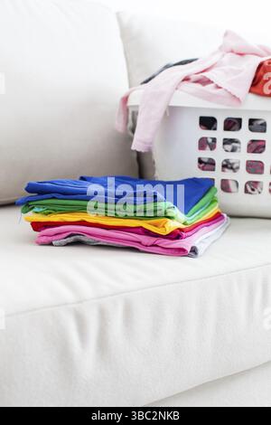 Washed clothes in a basket and stack of clean linen on the sofa Stock Photo