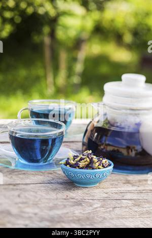 Two transparent cups and a teapot filled with blue matcha tea are standing on a wooden table Stock Photo