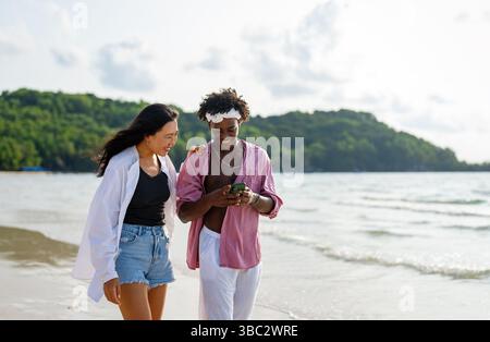 Trendy digital creator couple taking selfie by the beach, sharing travel content for social media Stock Photo