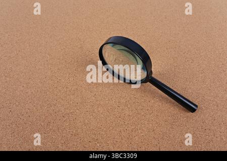 Magnifying glass placed on a cork board background. Idea for searching, detective work or typing text Stock Photo