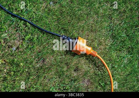 Black and orange extension cord plug connected on grass lawn in sunlight. High quality photo Stock Photo