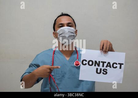 Young doctor man holding paper with text contact us Stock Photo