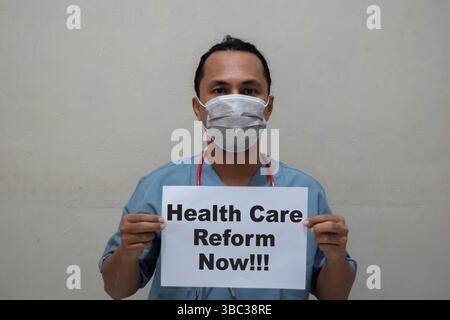 Young doctor man holding paper with text Health care reform now! Stock Photo
