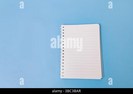 An open spiral notebook with lined white pages isolated on light blue background. The clean, minimal design is ideal for use in educational, planning, Stock Photo